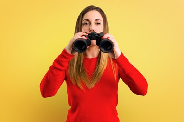 Obraz premium Young blonde woman with binoculars on yellow background