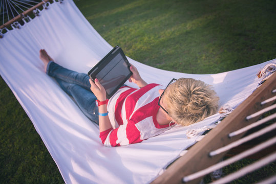 woman using a tablet computer while relaxing on hammock