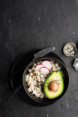 A simple lunch bowl with wild and brown rice, avocado halves, radish slices for a healthy diet. Top view. On a dark background.