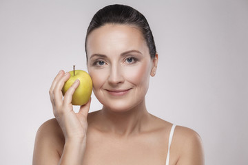 Portrait of charming beautiful healthy caucasian middle aged woman holding green apple, she love to eat fruit, make her get good health, nice skin, lose weight and weight control. Copy space, indoor