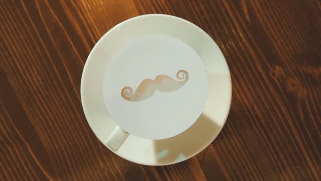 drawing on the foam of coffee or latte art in the form of a mustache close - up in the barbershop