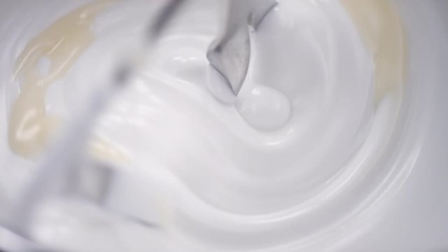 Blender whiskes white cream while beige liquid is added in the laboratory