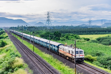 awesome close front engine view of indian railway running on track goes to horizon in green landscape under blue sky with clouds. - 241752182