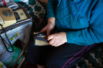 Old poor gray hair woman holds Ukrainian hryvna money in her hands. Woman is sad. Poor life in village. Old age not good. Low-light photo.