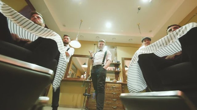 three professional Barber or hairdresser satisfied with the result of their work twist chairs with customers with beautiful stylish haircuts and beards, smile and twist in the hands of scissors