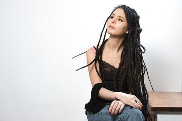 Obraz premium Cute dreaded hipster girl wearing a black top and blue jeans posing on a staircase against a white background.