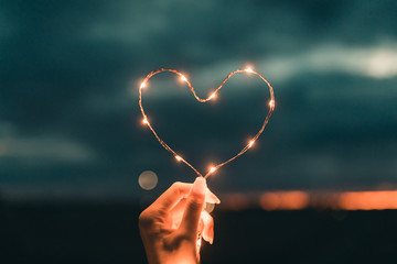 Simbolo del cuore fatto da una striscia di luci led tenuto da una mano di una ragazza di fronte al cielo sfuocato. San Valentino concetto.