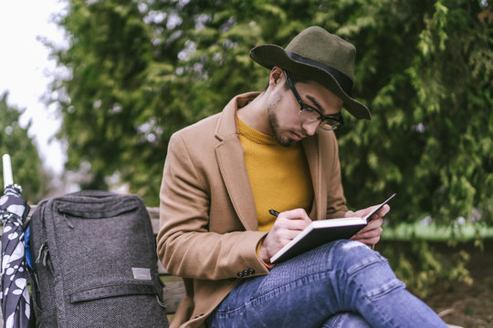 Young man writing in diary while sitting outdoors