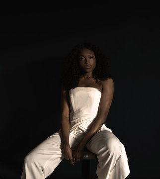 Young woman sitting on stool against black background