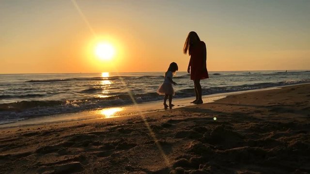 Silhouette video of mother and daughter walking along the beach at sunset. 