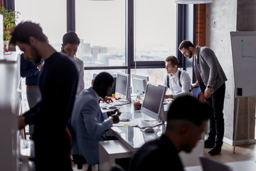 Multi Ethnic group of male architectures and web-designers standing randomly in the big spacious open space office with modern loft interior and computer desks. Routine working process.