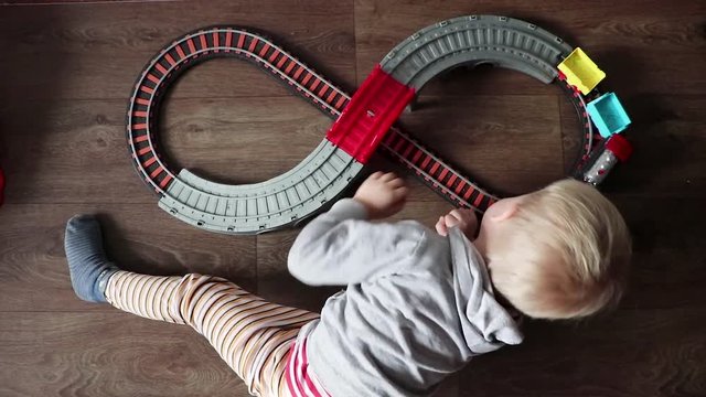 A little boy plays a children's railway. Mom is watching her son from above. The child is fascinated by the train
