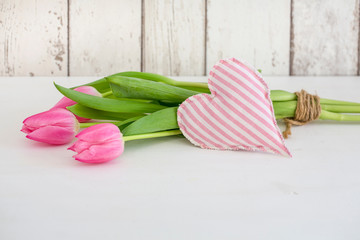 Feminine spring still life with pink tulips and fabric heart in front of wooden panel with copy space