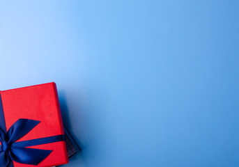 Fototapeta premium Red box gift with blue ribbon on blue background, top view fashion flat lay