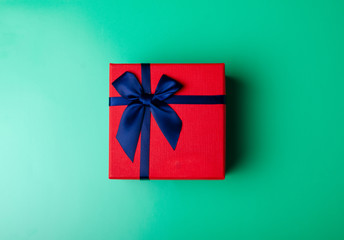 Red box gift with blue ribbon on green background, top view fashion flat lay