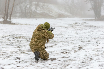 Naklejka premium A military soldier in camouflage with a weapon goes on the offensive in winter.