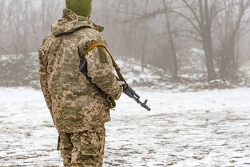 A military soldier in camouflage with a Kalashnikov assault rifle is waiting for an order.