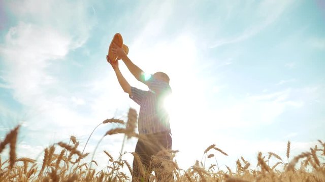 old farmer man silhouette baker holds a golden bread and loaf in ripe wheat field against the blue sky. slow motion lifestyle video. successful agriculturist in field of wheat. harvest time. old man