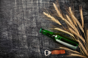 A bottle of beer with spikelets and opener on a black scratched chalk board