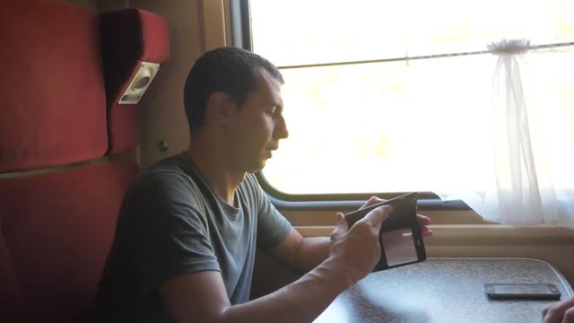 man traveler Relaxing On Train Listening To Music and smiling through the pictures via social media. slow motion video . uploading lifestyle photo using cell phone while riding home by train wagon