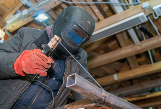 welder holds electrode in his hands and welds pipe in helmet.