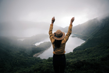 woman traveler holding hat and looking at amazing mountains and forest, wonderful travel concept,...