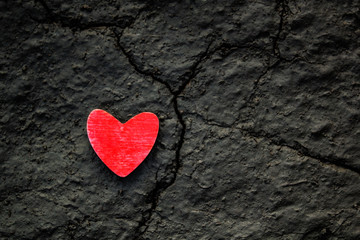 Red wooden heart on a cracked dry grey ground. Broken up heart life concept