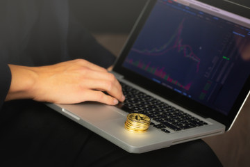 Businessman working on laptop with a golden bitcoin coins stack on it. Exchange chart on screen.