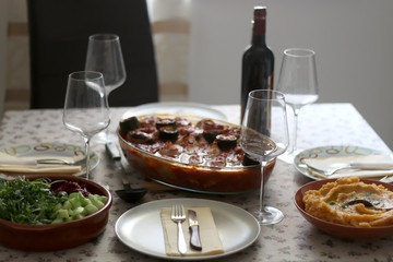 Table setting with four places, roasted vegetables with tomato sauce, salad and mashed sweet potato and wine. Selective focus, moody lighting.