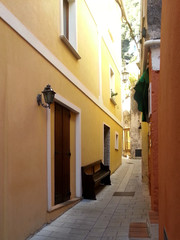 Fototapeta na wymiar A narrow street between the houses and a brown bench in Maratea, Basilicata, Italy