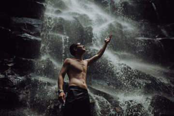 Fototapeta na wymiar lean muscular Man look up on waterfall in dark