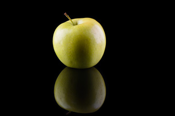 Green apple variety Golden on a black background with reflection