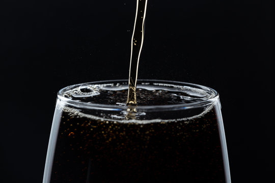 A glass of cola beverage with a salt. On a black background.