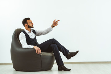The businessman sitting on a bag chair on a white wall background and gesturing