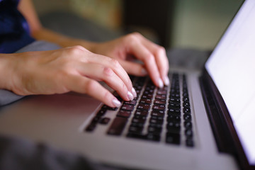 Close-up of woman's hand using laptop with blank screen on bed in home interior. The light from the screen illuminates the female hands on the laptop keyboard. Freelancer works at home in the evening