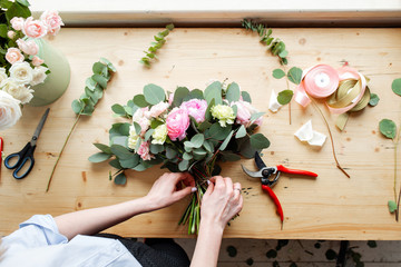 Close-up of hand Professional florist making a bouquet of pink Ranunculus and peonies in a flower...