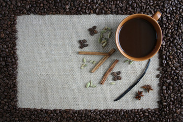 A border of coffee beans, inside on a fabric of jute a cup of black coffee, a biscuit cake and spices: cardamom seeds, cinnamon sticks, vanilla and star anise
