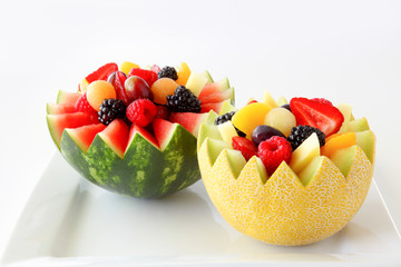 Fancy cut melon and watermelon with assorted fruit inside on a white background