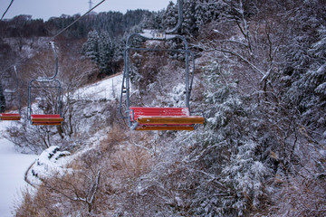 Empty orange chair on lift heading up snowy mountain
