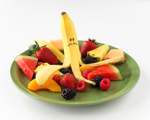 Banana with funny face on plate of fruit