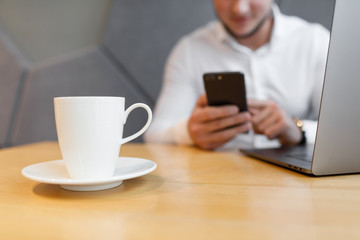 Portrait of Young man with a mobile phone sitting at cafe using laptop.