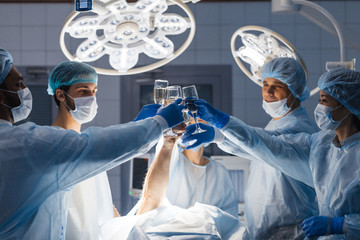 Cheerful team of surgeons congratulating each other with New Year, cheering with glasses of non...