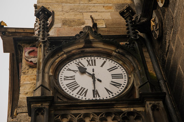 Closeup photo of a medieval clock on the wall of a very old brown historical building