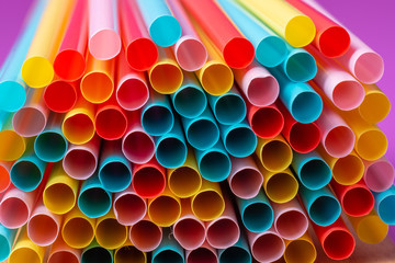 Close up end view of colorful plastic straws laying on the side with a purple background.
