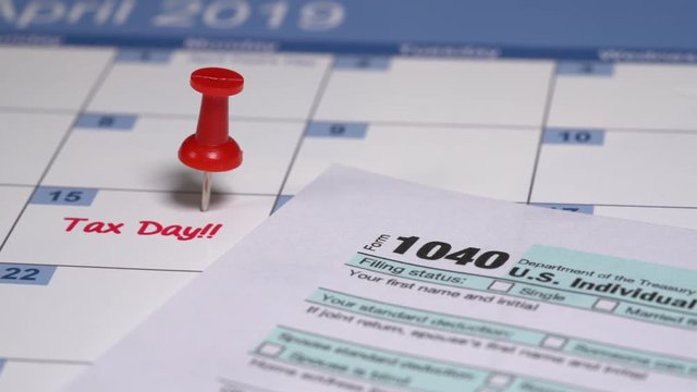 Slow rotation with dolly around the title of the 2018 simplified form 1040 for US tax returns due on April 15, 2019 with a pushpin in the date