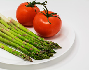 Fresh organic asparagus shoots two red tomatoes on a branch on white background