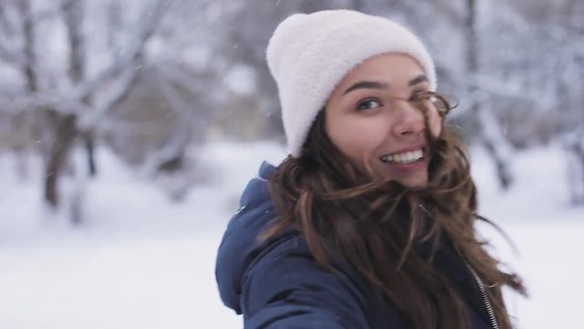 Atractive beautiful brunette woman runs away in snowy park. Follow me