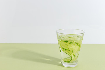 Glass cup with cucumber water on a light green background. Minimalistic creative concept. Copy space.