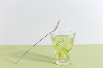 Glass cup with cucumber water on a light green background. Minimalistic creative concept. Copy space.