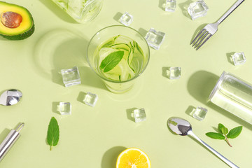 A glass beaker, a bottle of cucumber water, fruits and cutlery on a light green background. Minimalistic creative concept. Copy space.